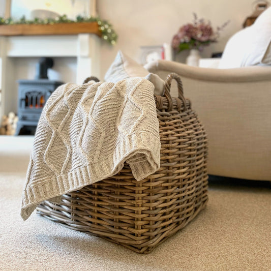 Soft melange grey chunky cable knit throw with ribbed edge draped over an armchair in a calm, cosy living room.