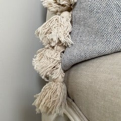 Grey textured cotton cushion with cream tassels on each edge.
