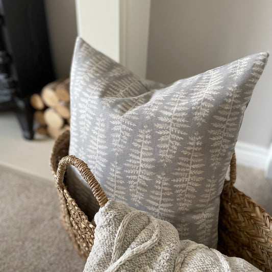 Dove grey cushion with beige and white leaf pattern styled in a seagrass basket with a throw.