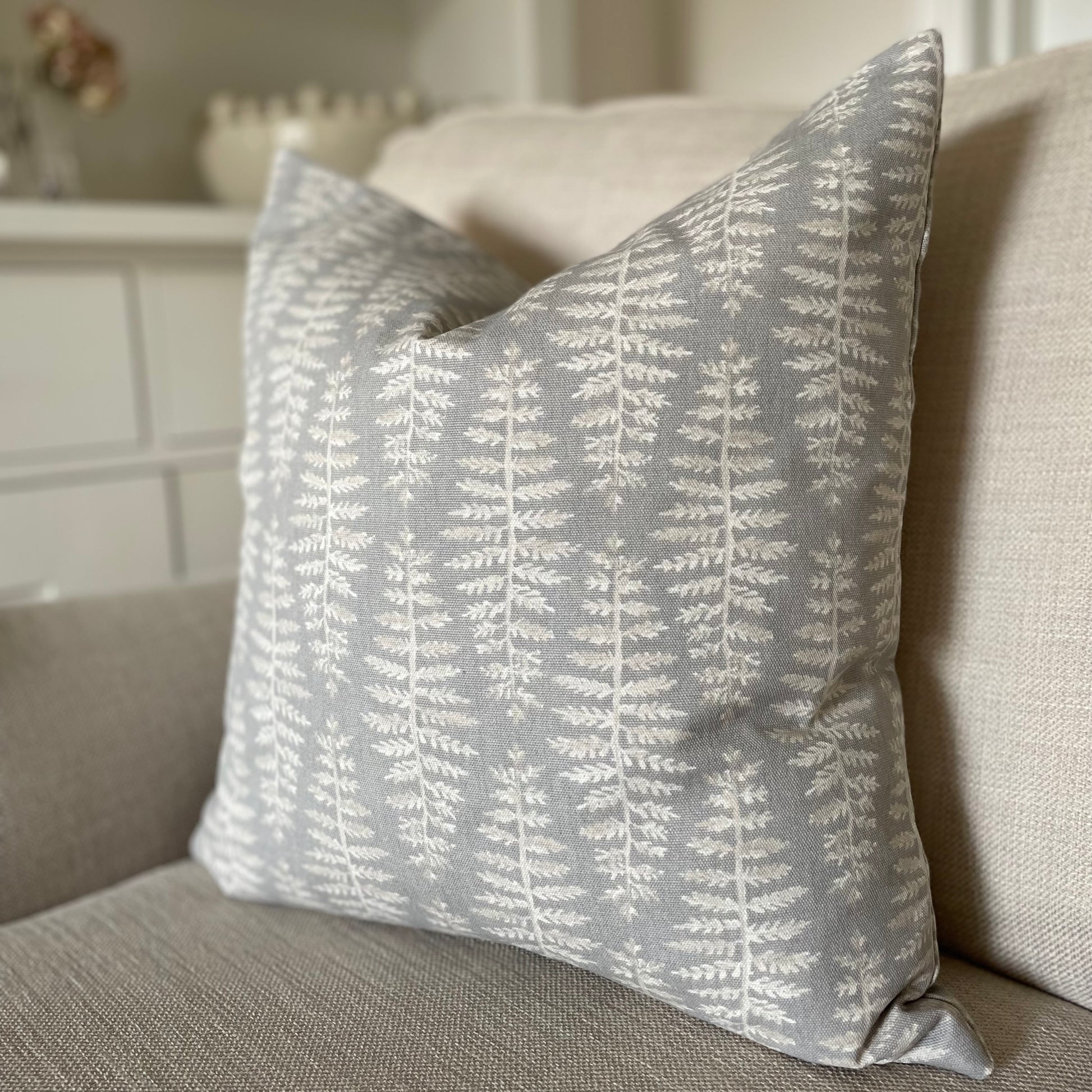 Dove grey cushion with beige and white leaf pattern styled on a neutral armchair.