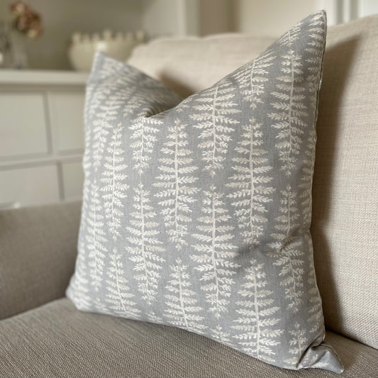 Dove grey cushion with beige and white leaf pattern styled on a neutral armchair.