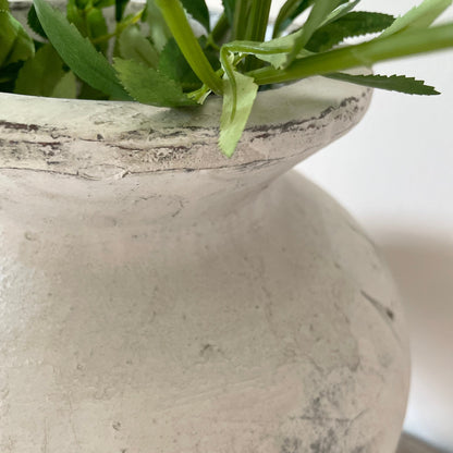 Close up of a textured stone vase with green leaves inside
