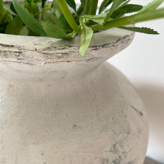 Close up of a textured stone vase with green leaves inside