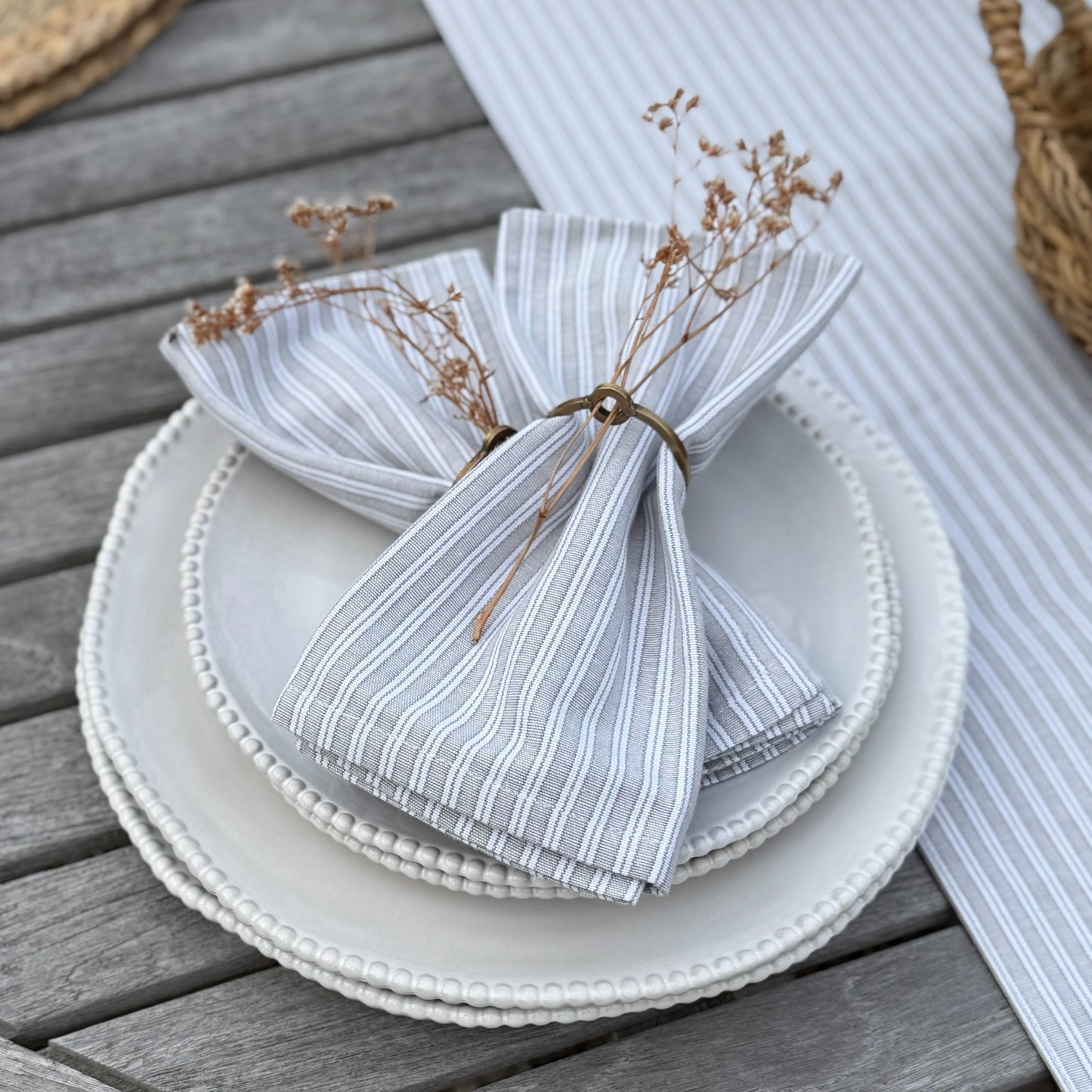 Stack of white plates with a folded striped napkin and dried flowers on a wooden surface.