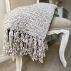 Grey soft textured throw with tassels, draped on a neutral chair.