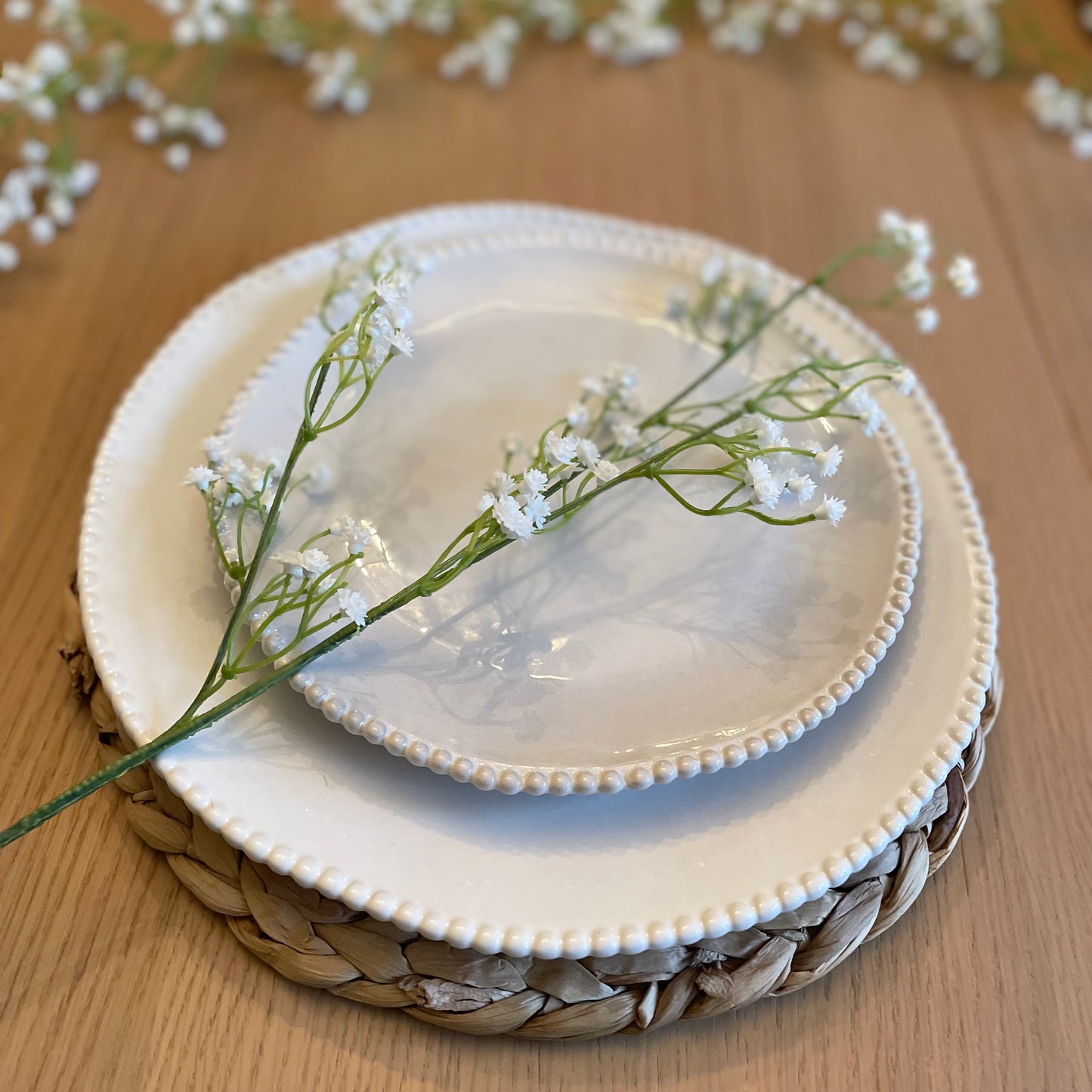 Faux white gypsophila stems arranged in a vase, styled on a plate and table.