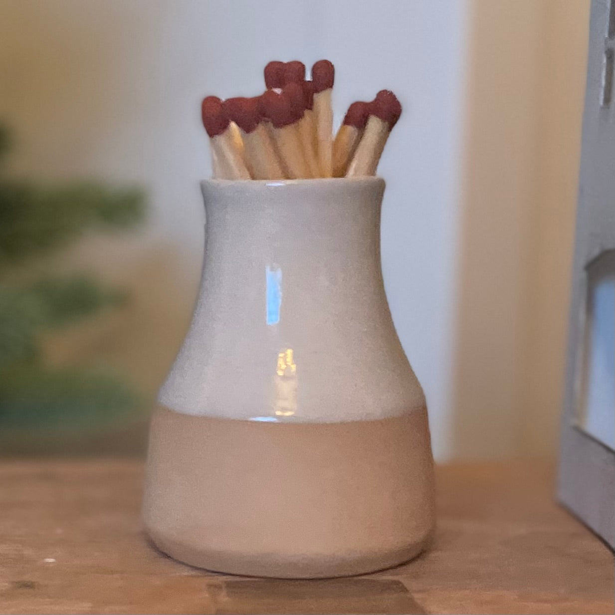 Handmade ceramic milk bottle match holder with long safety matches and hidden striker pad. Styled on a rustic table.