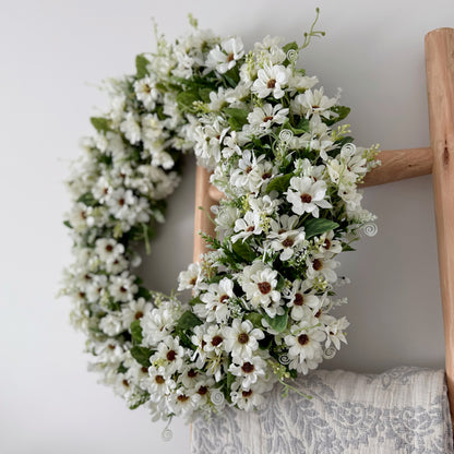 Floral daisy wreath on a wooden ladder against a white wall