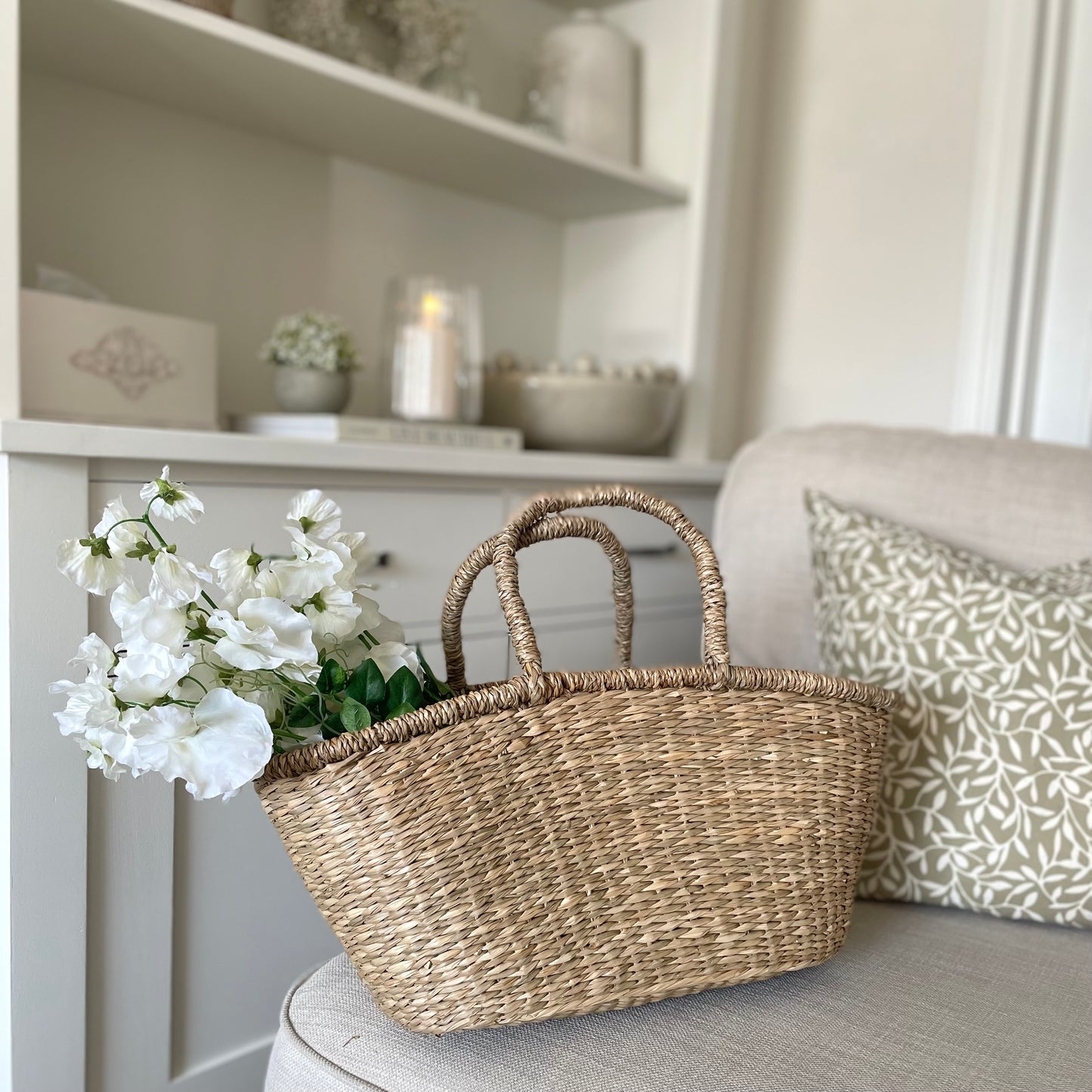 Handwoven seagrass shopper basket with natural texture, styled on a sofa in a cosy living room.
