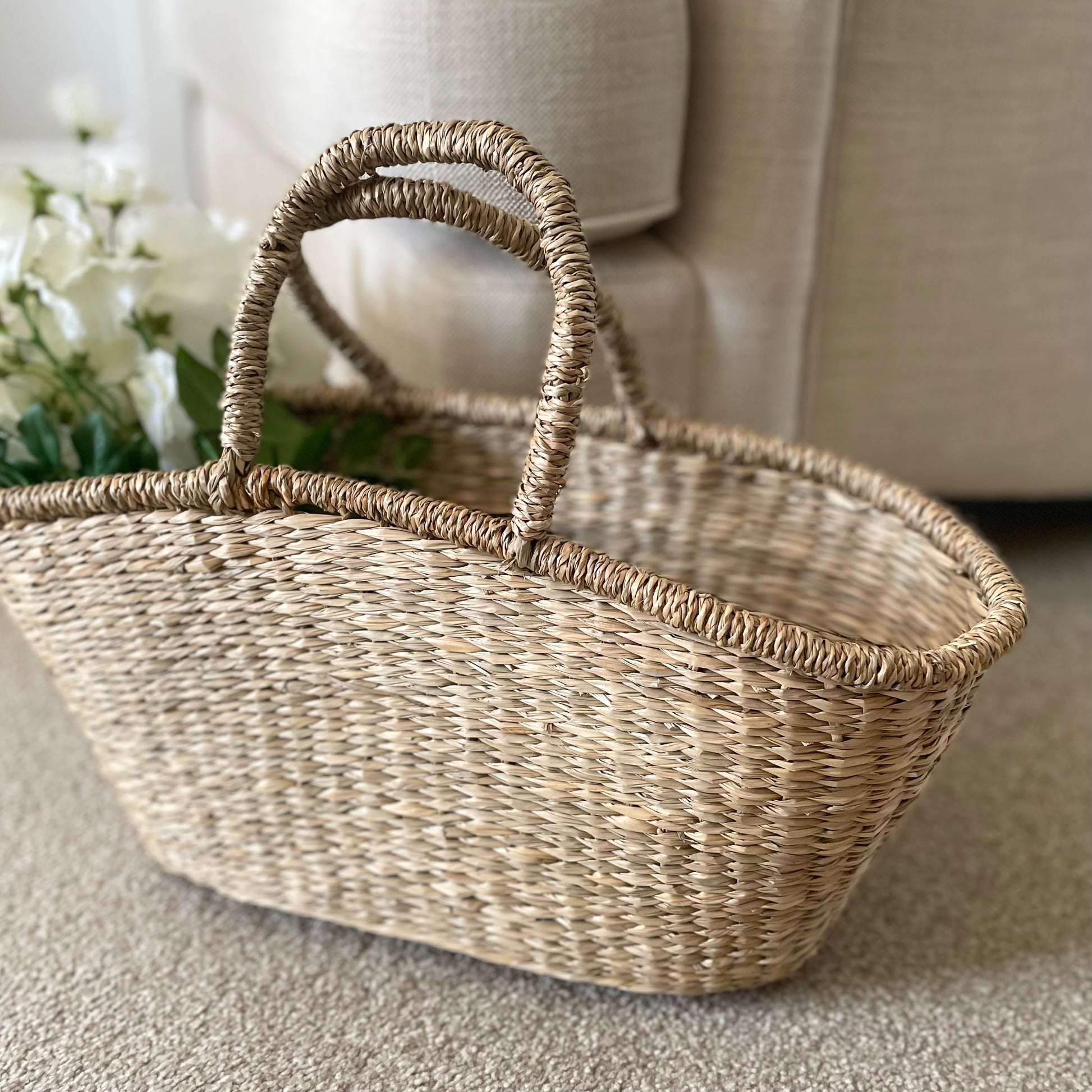 Seagrass shopper basket with woven handles styled with white sweet peas. Shown in a cosy living room.