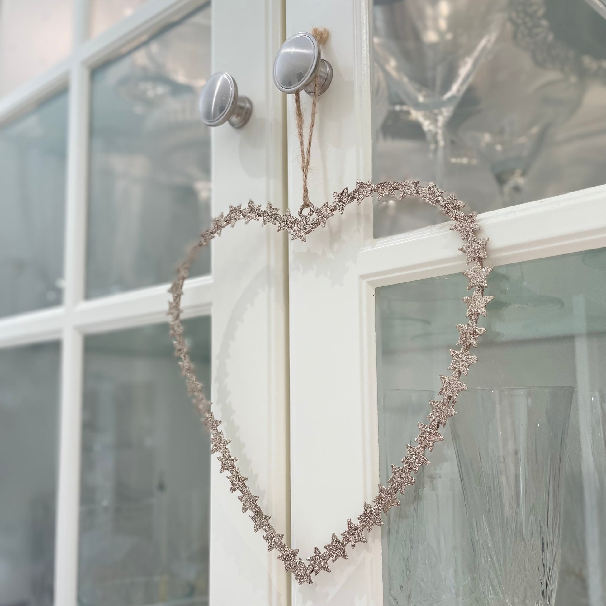 Heart shaped gold glitter star wreath hanging from natural jute string on a glass door.