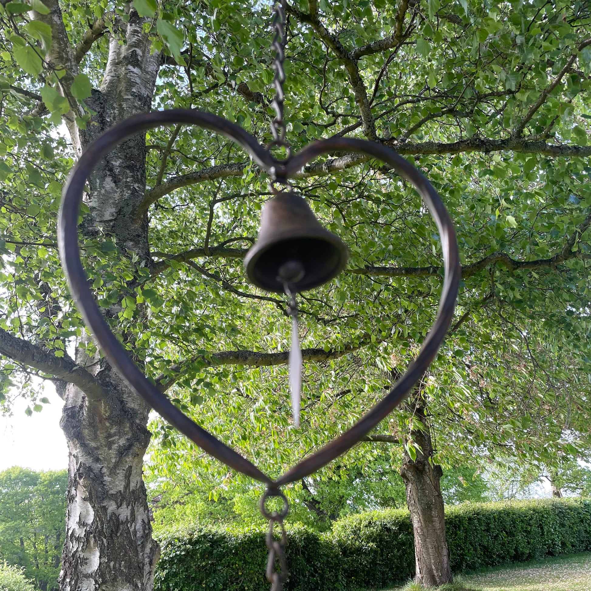 Handmade vintage style heart wind chime with delicate bells, hanging outdoors in a rustic garden setting.
