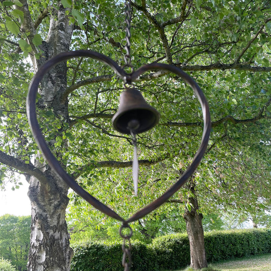 Handmade vintage style heart wind chime with delicate bells, hanging outdoors in a rustic garden setting.
