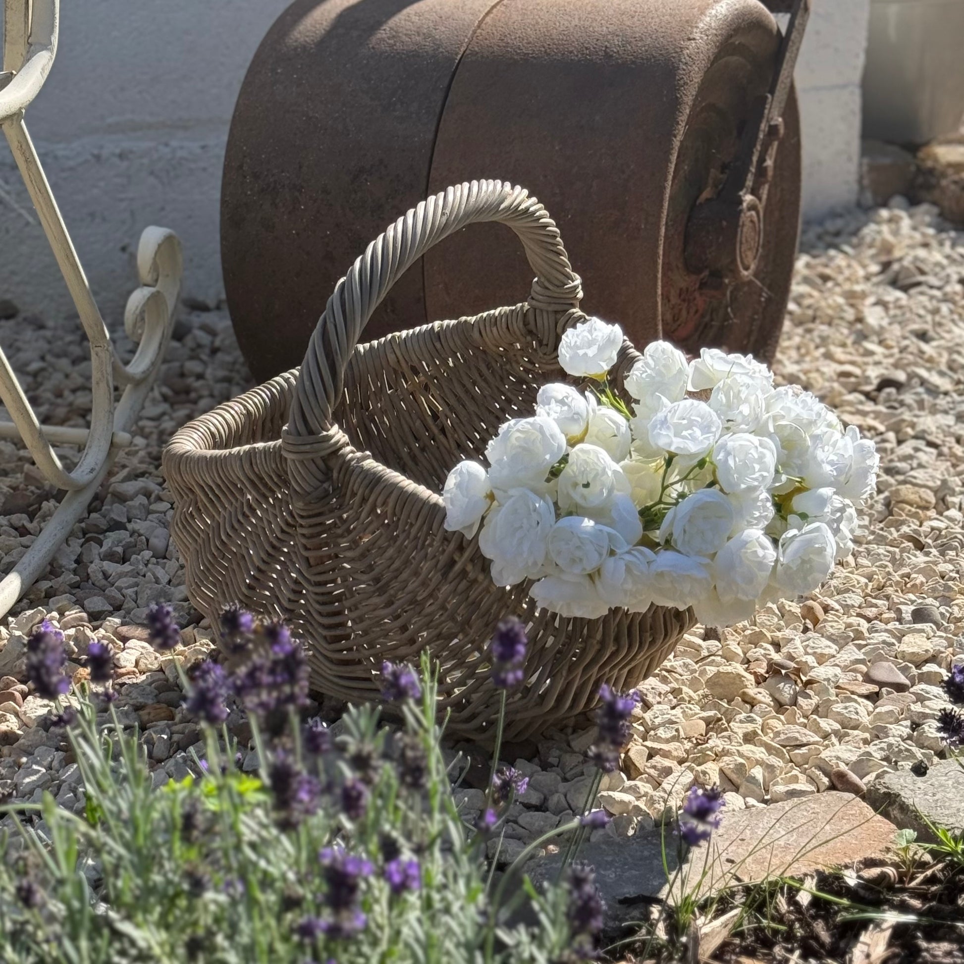 Wicker basket with white flowers on a stone surface with lavender plants. Handwoven rattan basket with circular easy carry handle. 