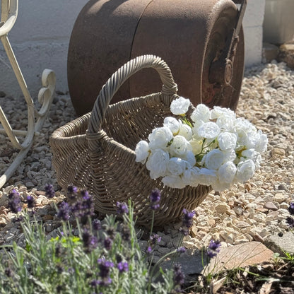 Wicker basket with white flowers on a stone surface with lavender plants. Handwoven rattan basket with circular easy carry handle. 