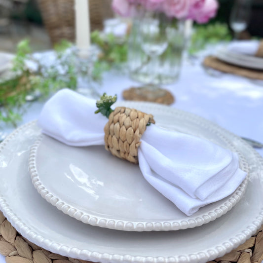 Woven hyacinth napkin ring holding a neutral linen napkin, showing its natural texture and rustic, organic finish. Styled on a garden dining table with a vase of pink roses.