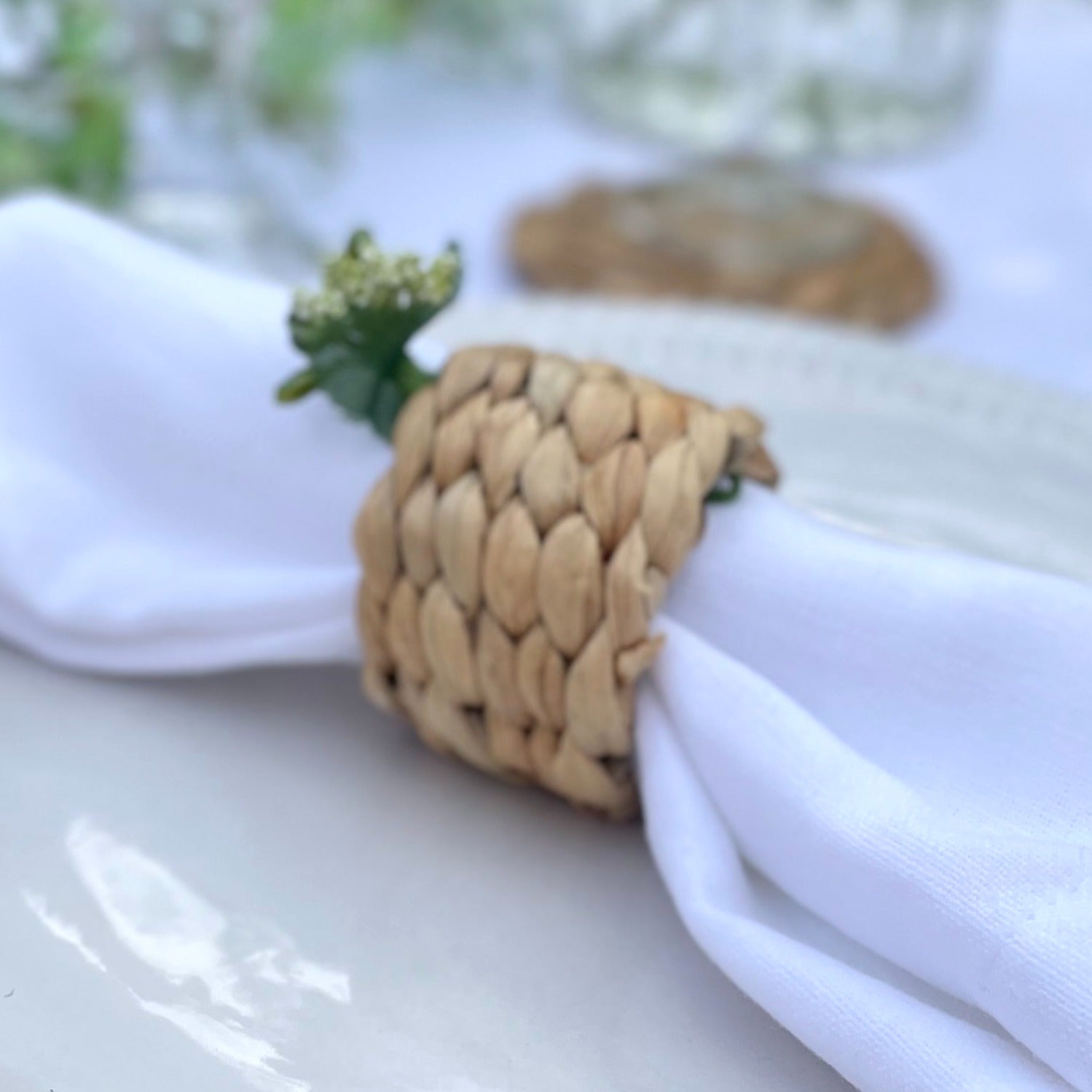 Woven hyacinth napkin ring holding a white linen napkin, showing its natural texture and rustic, organic finish. Styled on a dining table.