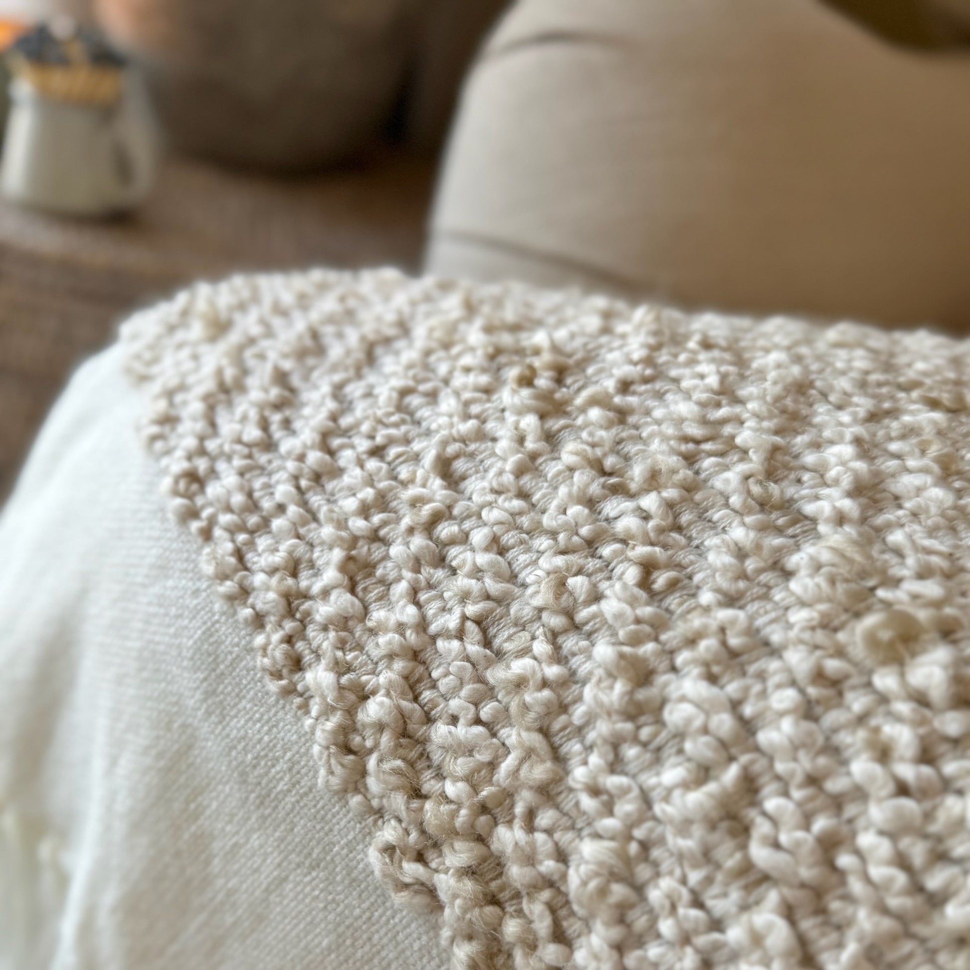 Knitted soft beige and white throw draped on a sofa.