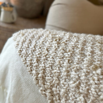 Knitted soft beige and white throw draped on a sofa.