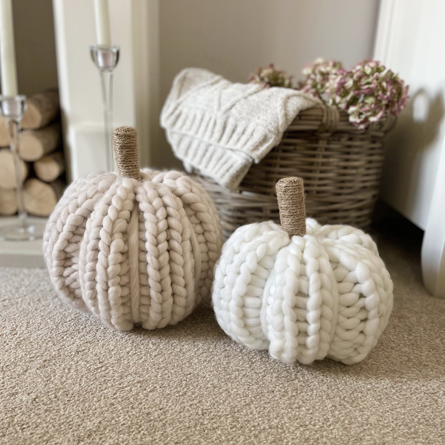 White and beige chunky knitted pumpkins with twine stalks styled next to a rustic basket with cable knit throw and hydrangea flowers