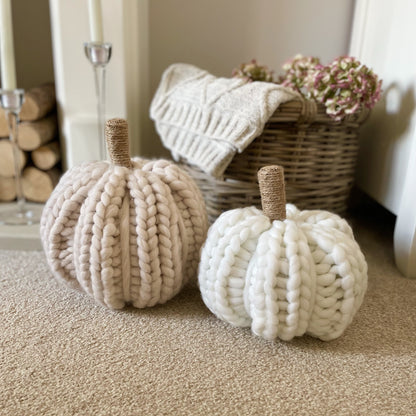 Oatmeal chunky knitted pumpkin with hessian twine wrapped stalk styled next to a basket and throw in a cosy living room..