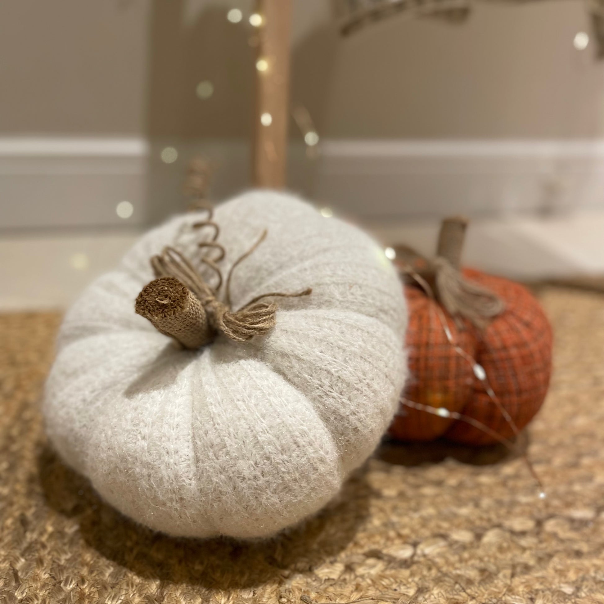Knitted white pumpkin with rustic hessian stalk styled on a wooden floor with autumn foliage.