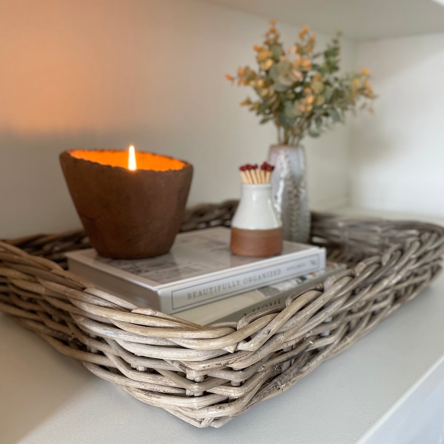 Handwoven natural rattan tray holding decorative items, adding warmth and texture to a neutral interior.