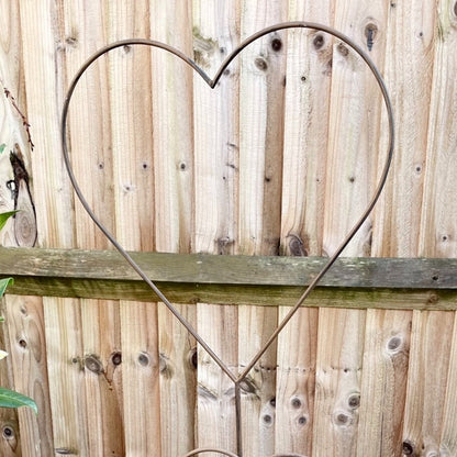 Rustic metal heart shaped garden stake with weathered finish, styled against a fence.