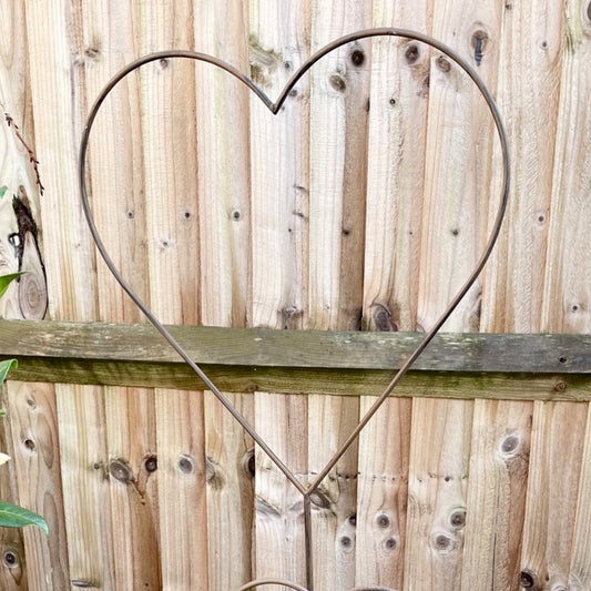 Rustic metal heart shaped garden stake with weathered finish, styled against a fence.