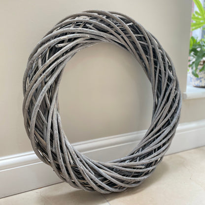 Grey white washed rattan large wreath with entwined design. Styled on a neutral background.