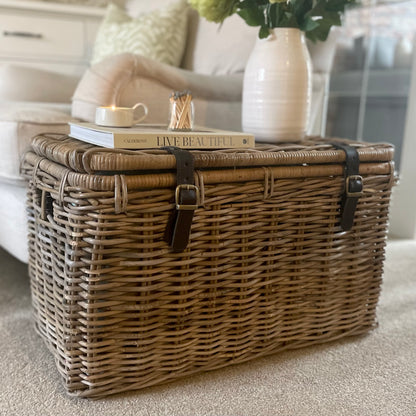 Natural woven trunk styled as side table in living room. With book, candle and vase of flowers.