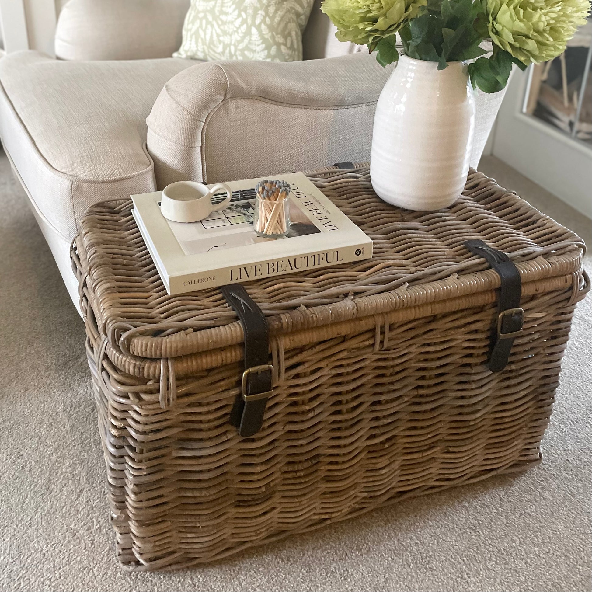 Natural woven trunk styled as side table in living room. Styled with a book, candle and vase of flowers.