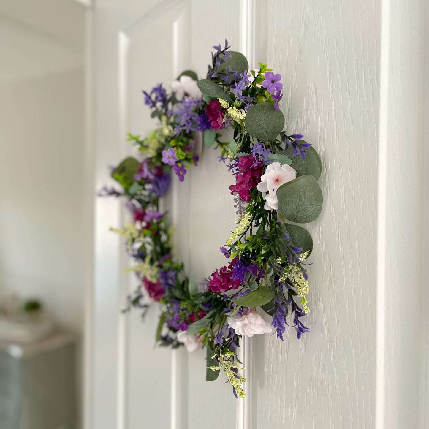 Faux lavender wreath with purple and white blooms, eucalyptus and peach wildflowers, 40 cm diameter styled on a white door.