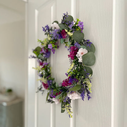 Faux lavender wreath with purple and white blooms, eucalyptus and peach wildflowers, 40 cm diameter styled on a white door.