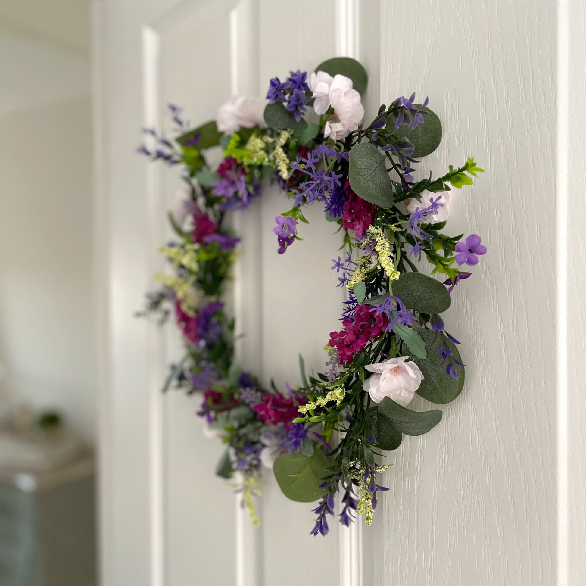 Faux lavender wreath with purple and white blooms, eucalyptus and peach wildflowers, 40 cm diameter styled on a white door.