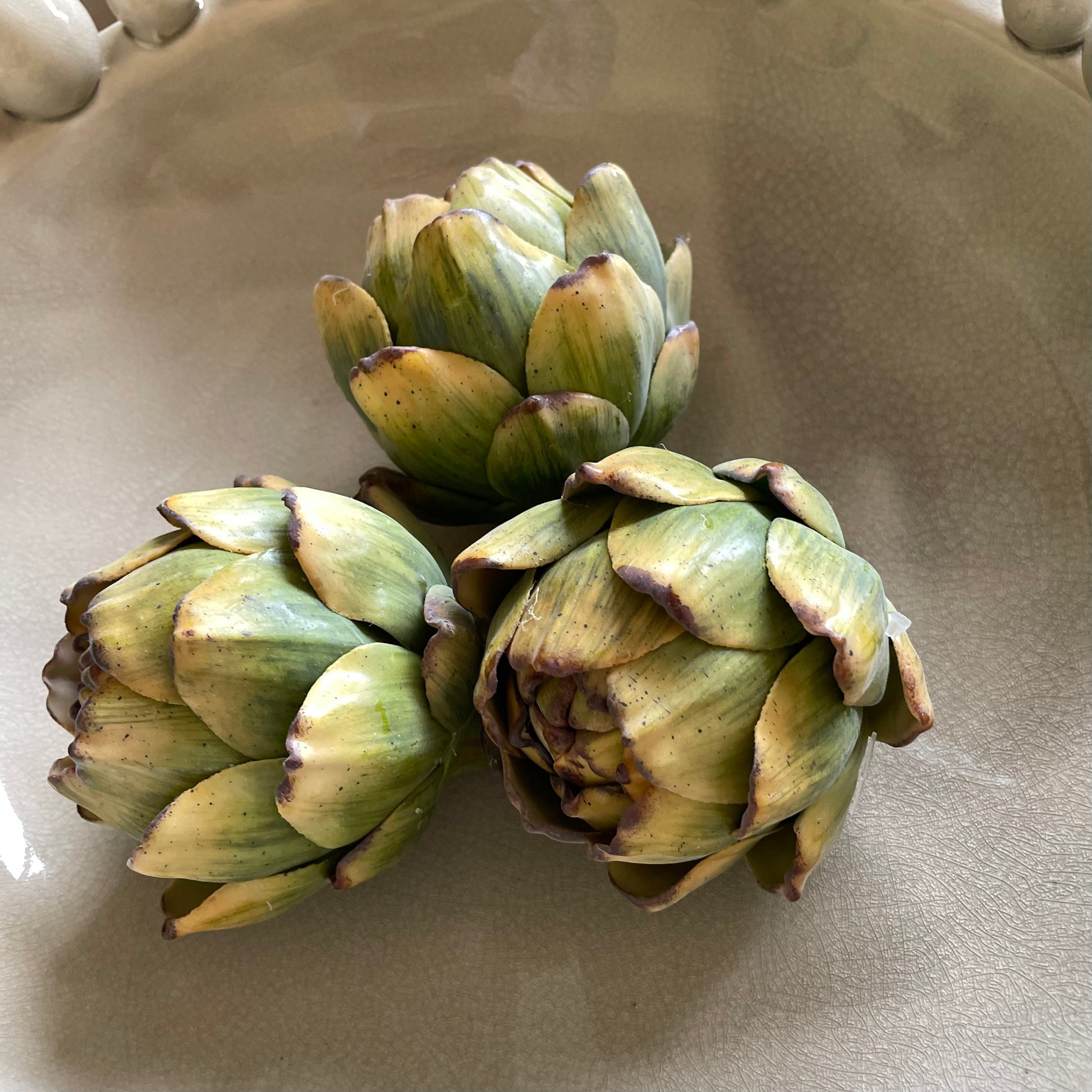 Natural looking artificial artichokes for decorative display. Styled in beige crackled glaze bobble bowl. Styled in a group of 3.