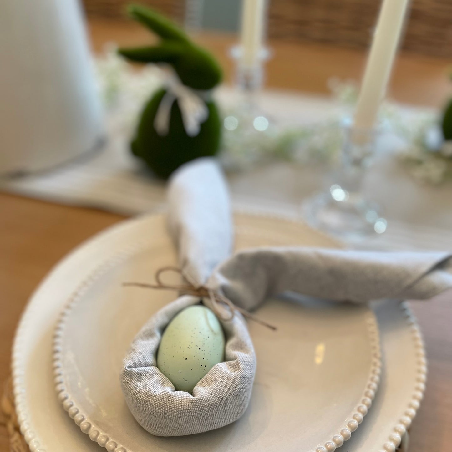 Set of four light grey cotton napkins neatly folded beside white porcelain plates on a dining table.