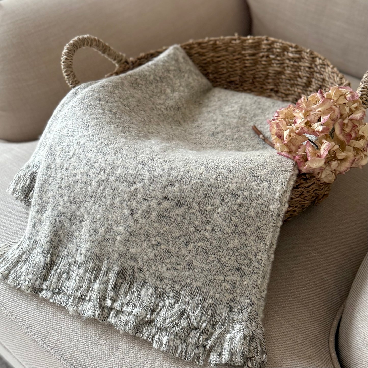 Gray textured throw blanket on a beige sofa with a woven basket and flowers.