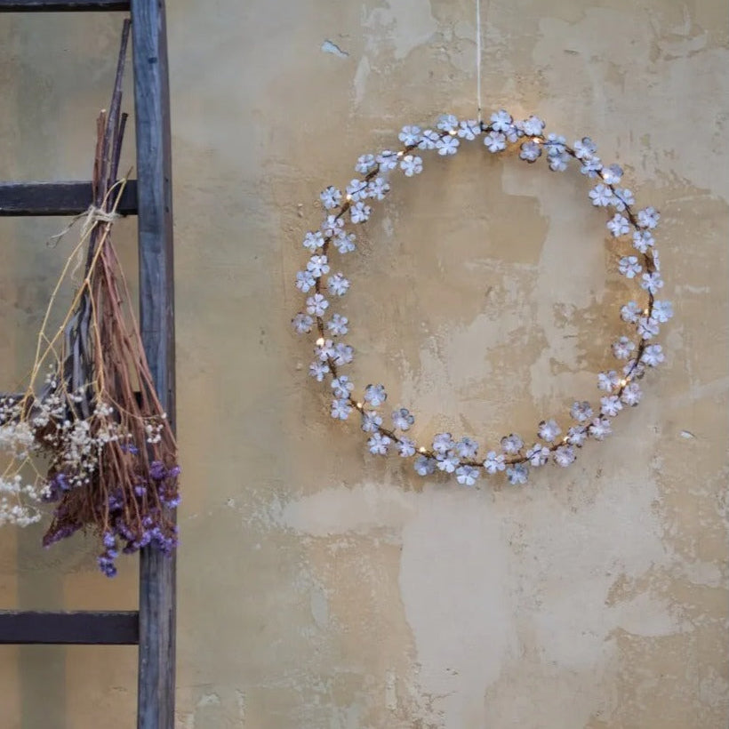 Dainty wildflower wreath with faded white leaves and warm white LED lights, hanging on a rustic wall with ladder.