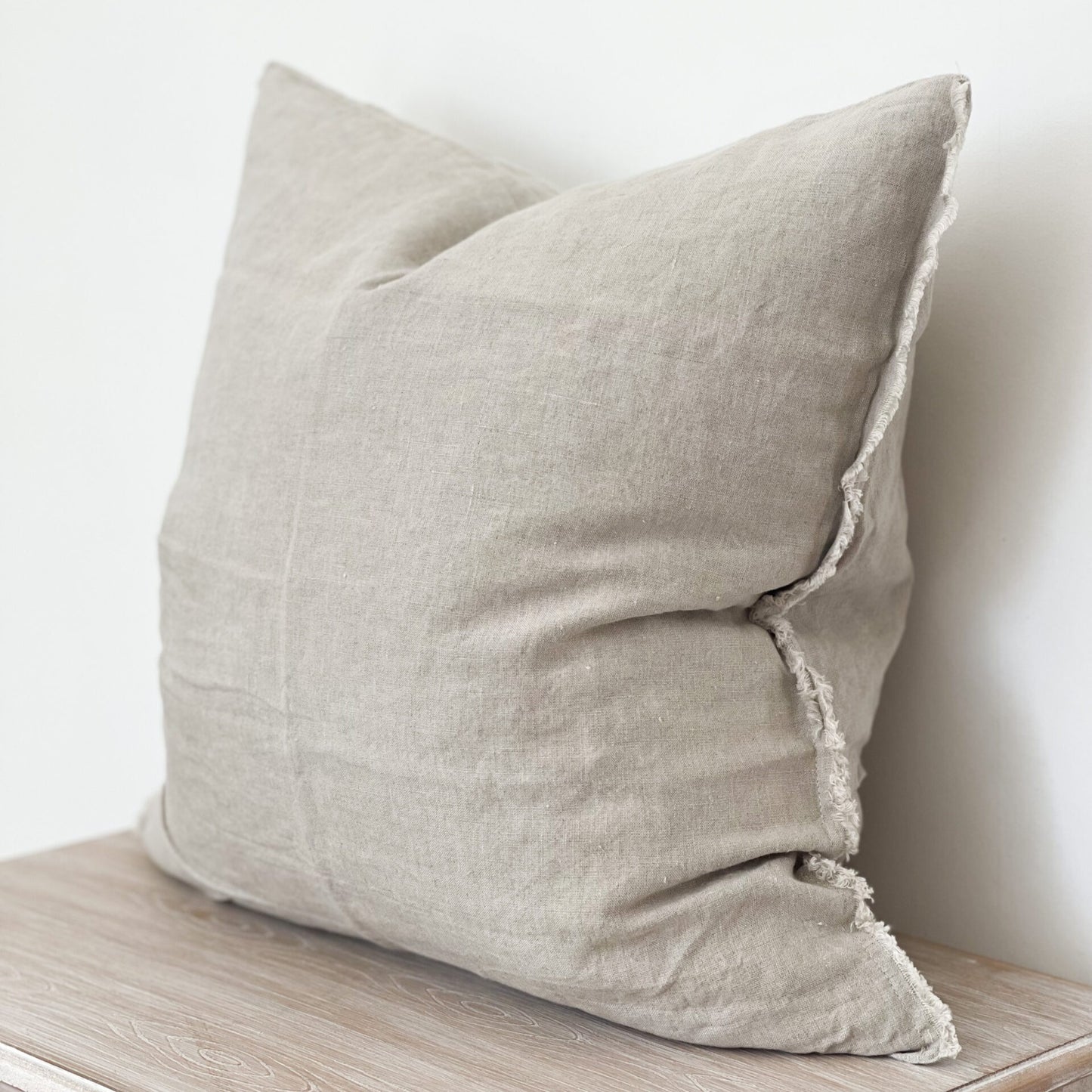 Linen sand cushion with frayed edges styled on a neutral sofa corner.