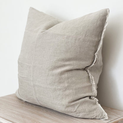 Linen sand cushion with frayed edges styled on a neutral sofa corner.