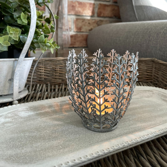 Metal leaf-effect tea light holder with glass insert, styled on a neutral wooden tray with a lit candle inside.