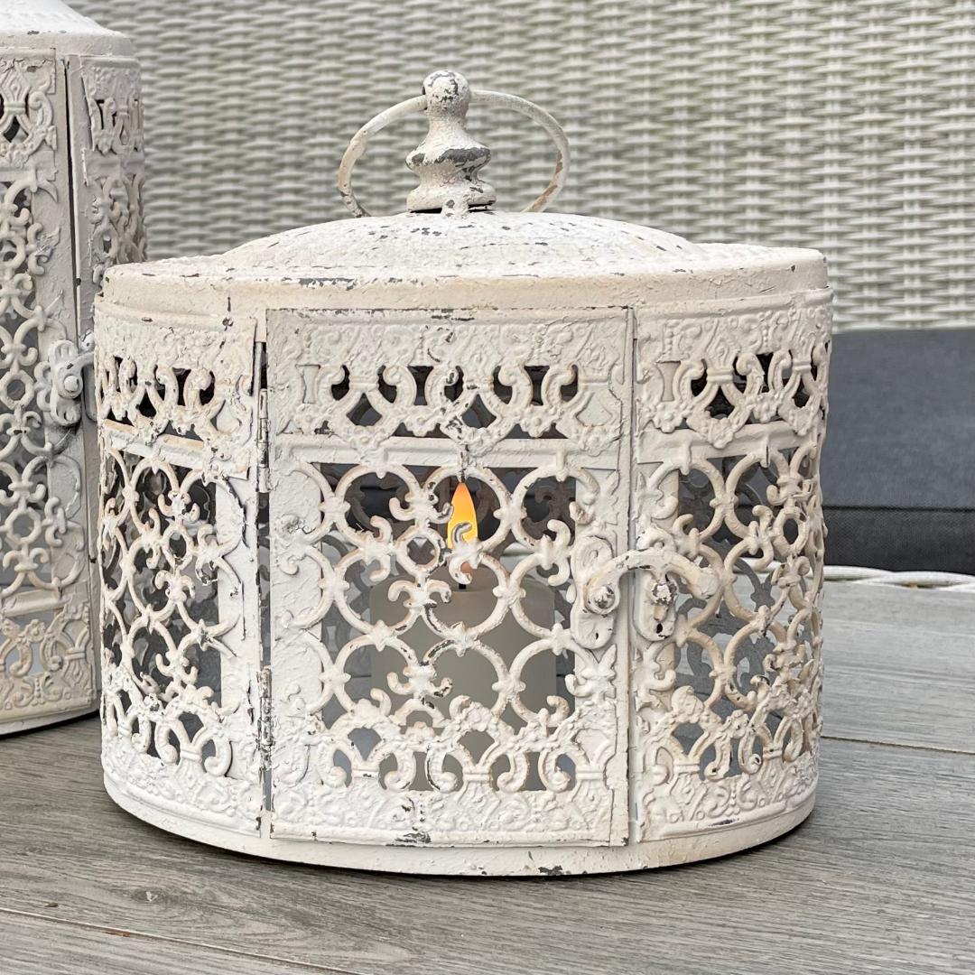 Antique white oval metal lantern with vintage finish casting soft candlelight.