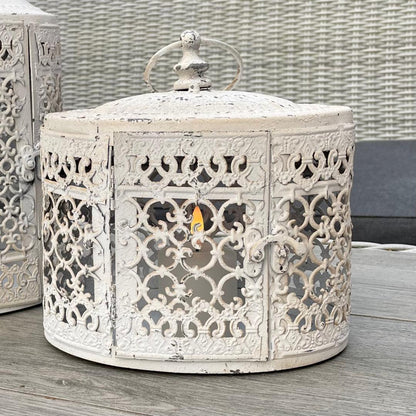 Antique white oval metal lantern with vintage finish casting soft candlelight.