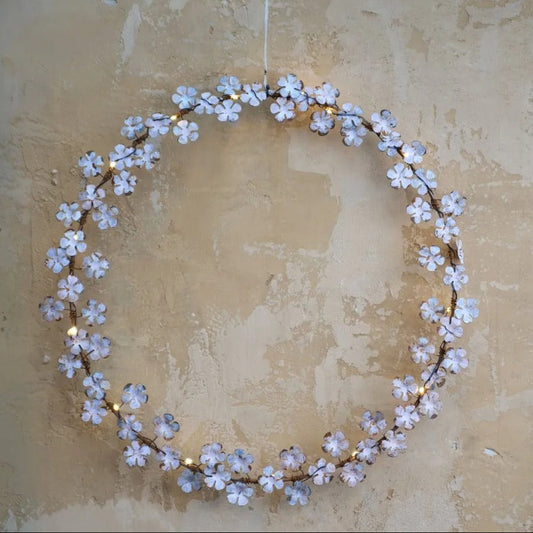Dainty wildflower wreath with faded white leaves and warm white LED lights, hanging on a rustic wooden door.