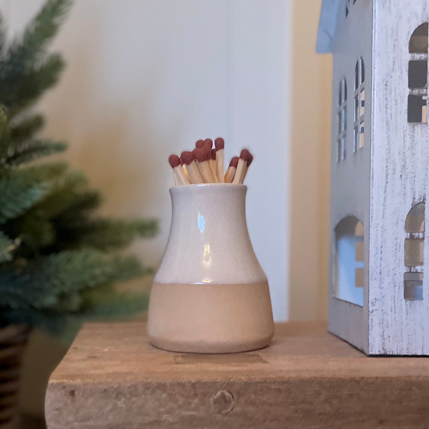 Handmade ceramic milk bottle match holder with long safety matches and hidden striker pad. Styled on a rustic wooden stool. 