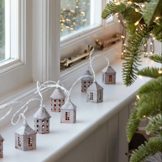Mini village house string lights illuminated with warm white LEDs. Styled on a country style windowsill.