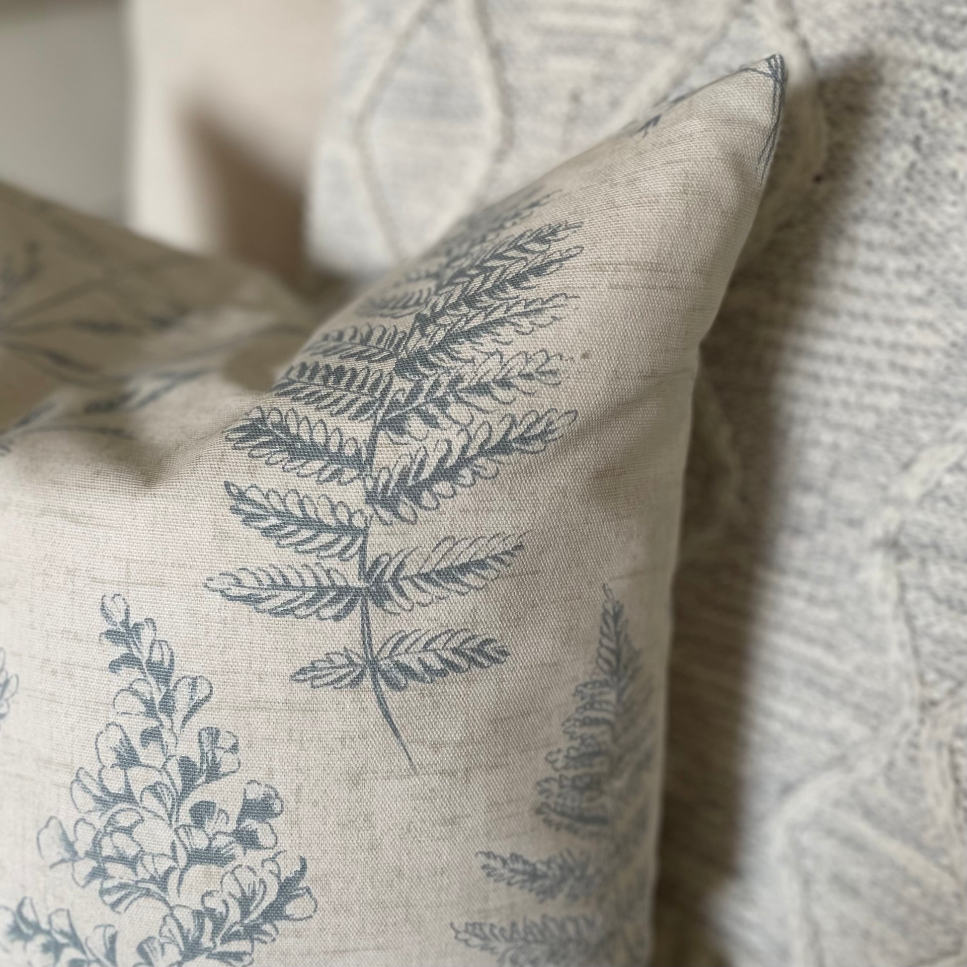 Natural cushion with blue leaf pattern styled on a neutral armchair with a throw.