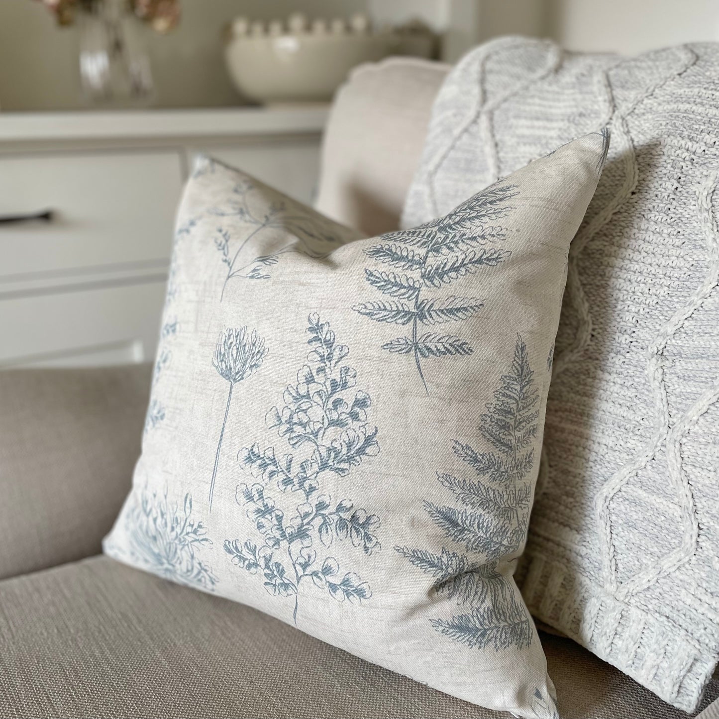 Natural cushion with blue leaf pattern styled on a neutral armchair with a throw.