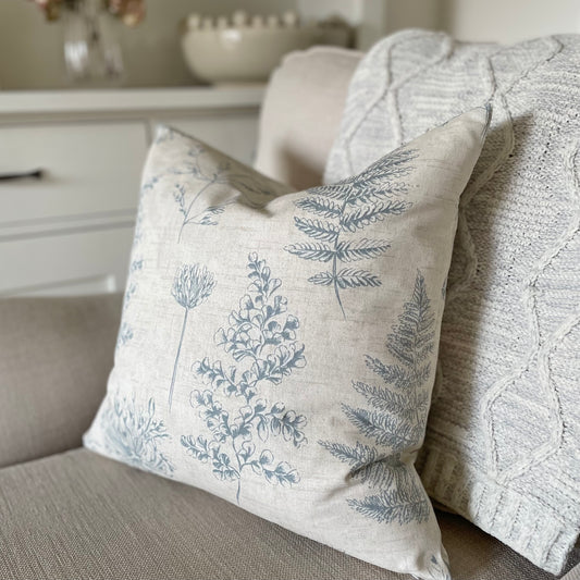 Natural cushion with blue leaf pattern styled on a neutral armchair with a throw.